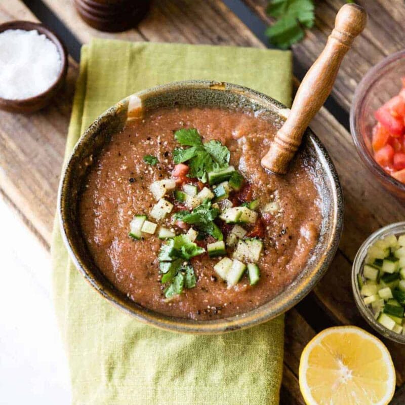 Blended easy gazpacho soup recipe in ceramic bowl on green cloth napkin.