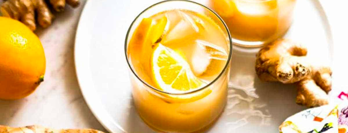 two glasses of orange/yellow drinks with ice cubes and lemon wedges
