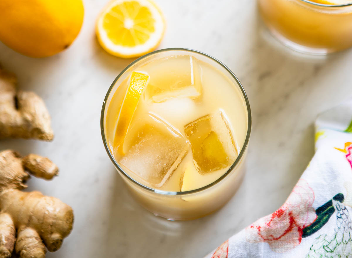 A glass of a ginger switchel recipe with ice cubes and a lemon wedge. 