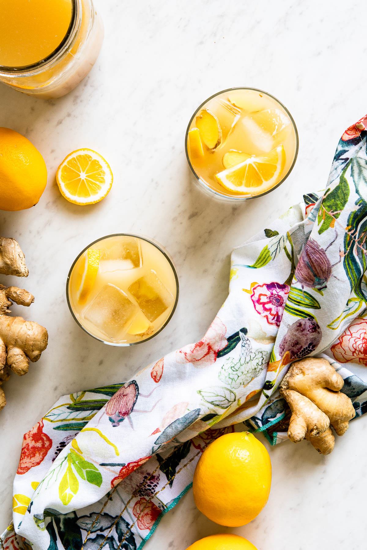 Two glasses, filled with ice and lemon wedges and a mason jar filled with ginger switchel recipe. 