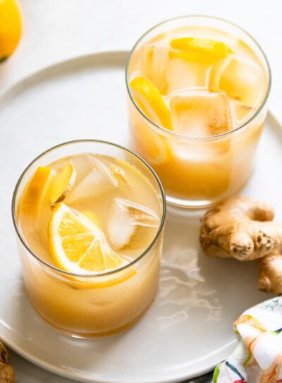 Two glasses of a ginger switchel recipe with ice cubes and lemon slices.