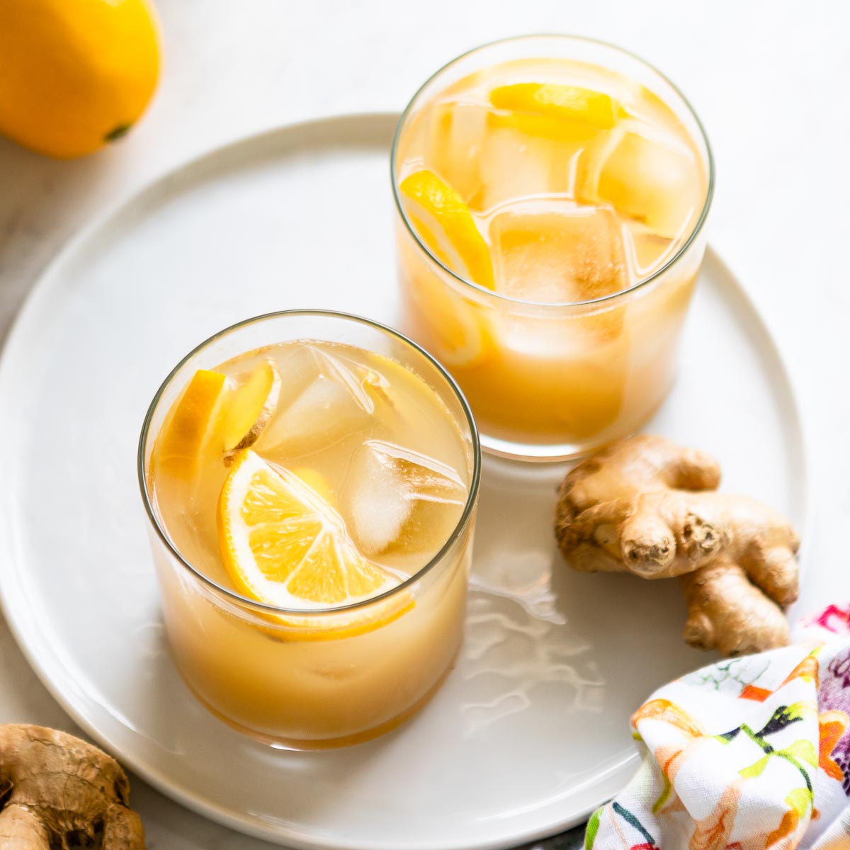 Two glasses of a ginger switchel recipe with ice cubes and lemon slices.