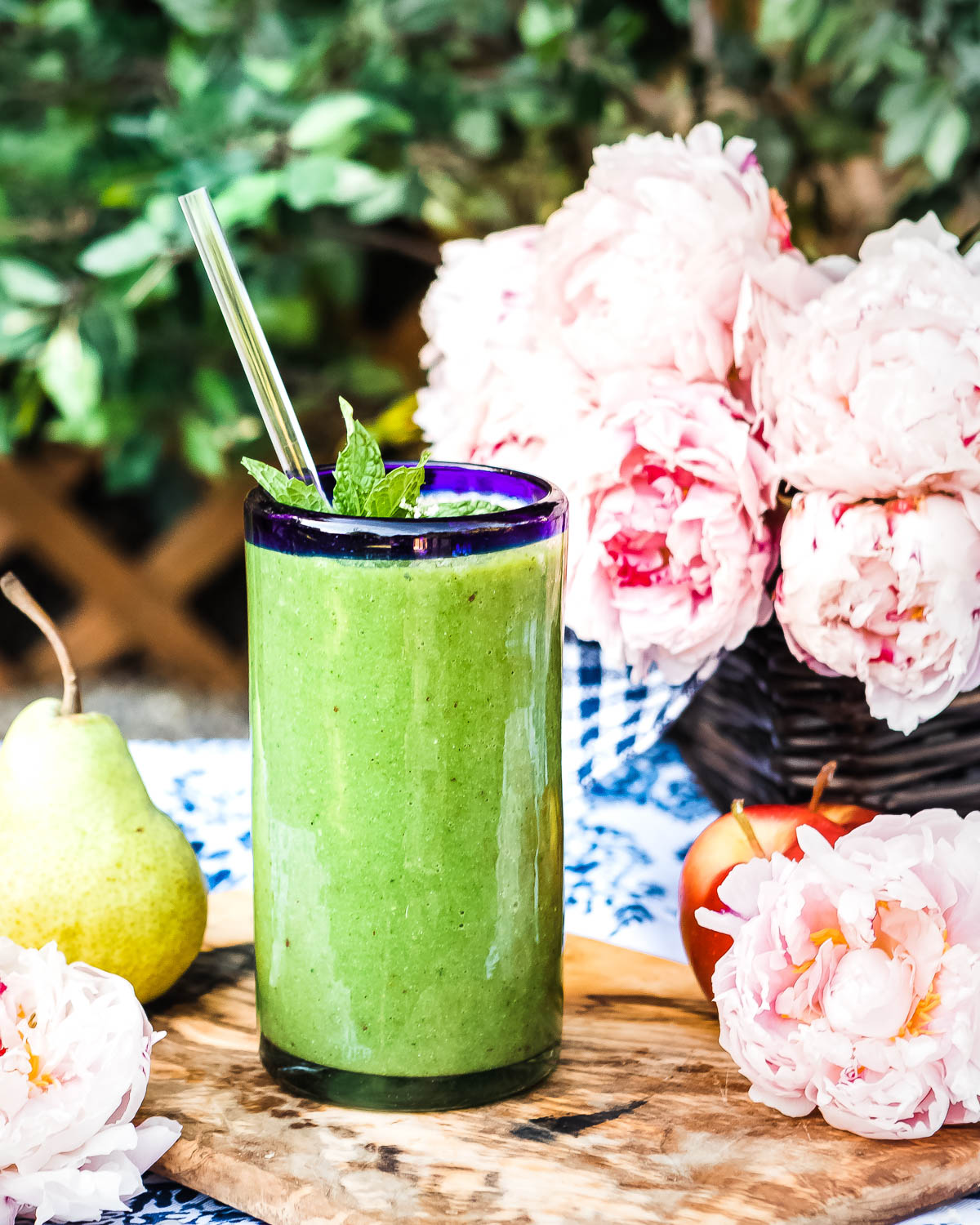 blue rimmed glass of glowing green smoothie with glass straw and fresh mint garnish.