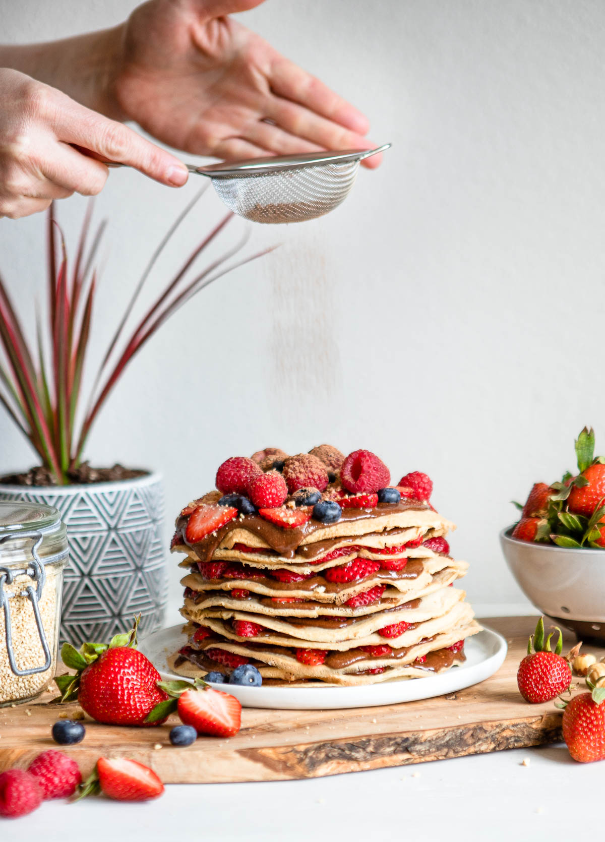 small colander sprinkling cacao powder over a stack of breakfast crepes 