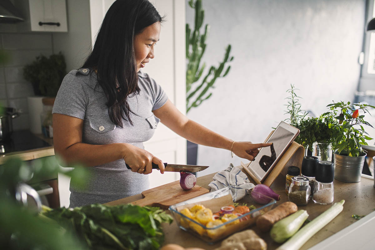 woman in a kitchen slicing a purple onion while consulting an ipad.