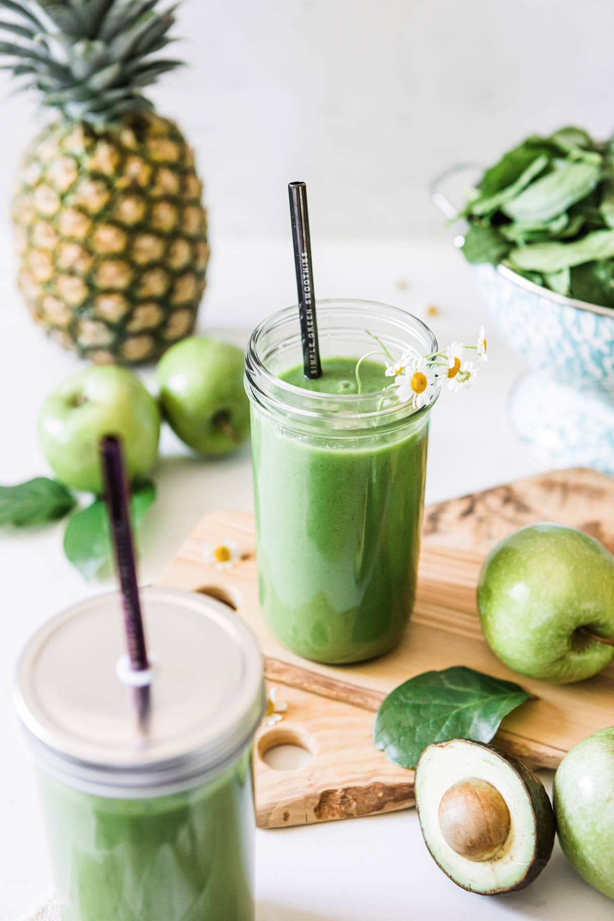 green apple smoothie in glass jar with apples, avocados and spinach surrounding it.