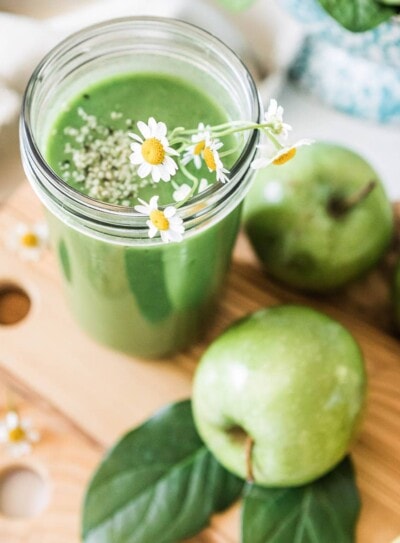 green apple smoothie in glass jar with floral garnish.