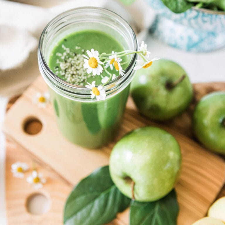 green apple smoothie in glass jar with floral garnish.