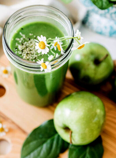 Green apple smoothie with hemp seeds and floral garnish in a glass jar, surrounded by fresh green apples.