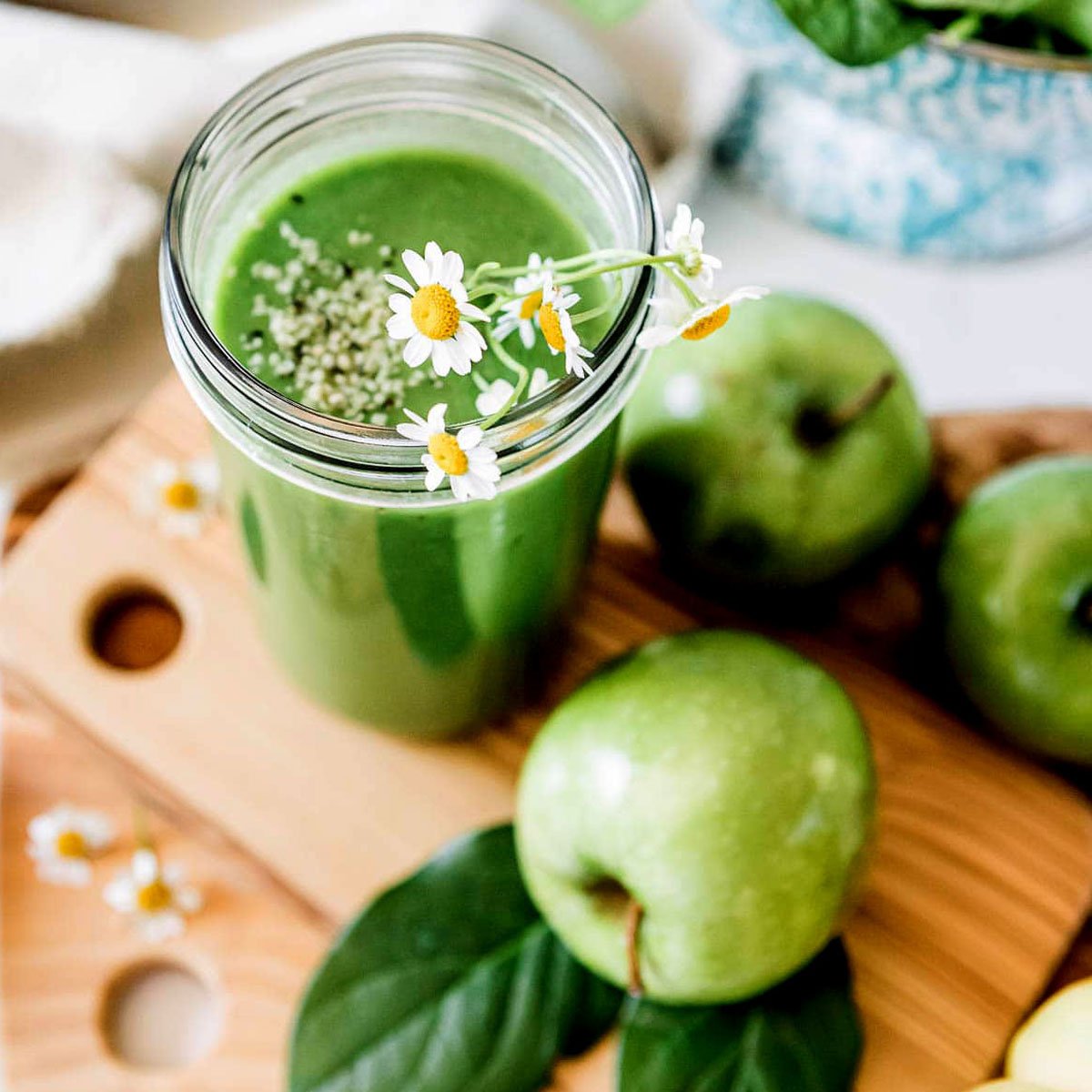 Green apple smoothie with hemp seeds and floral garnish in a glass jar, surrounded by fresh green apples.