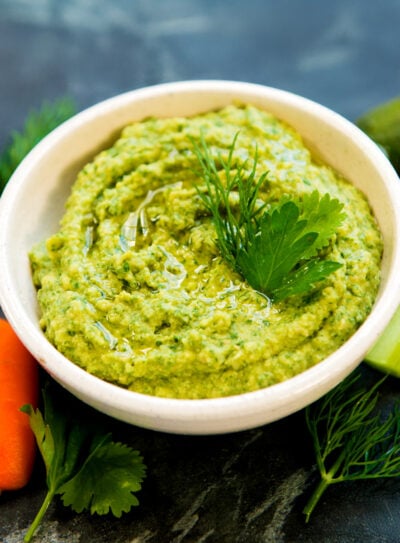Green goddess hummus in white bowl with carrot sticks and celery.