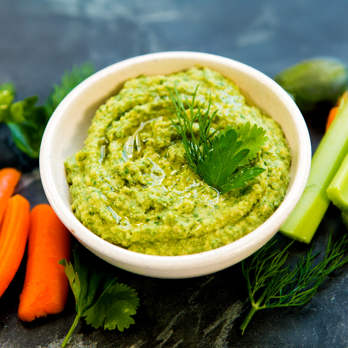 Green goddess hummus in white bowl with carrot sticks and celery.