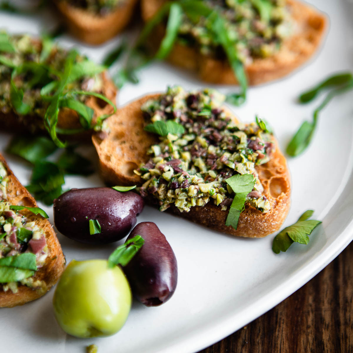 a white plate full of crostini topped with green olive tapenade.