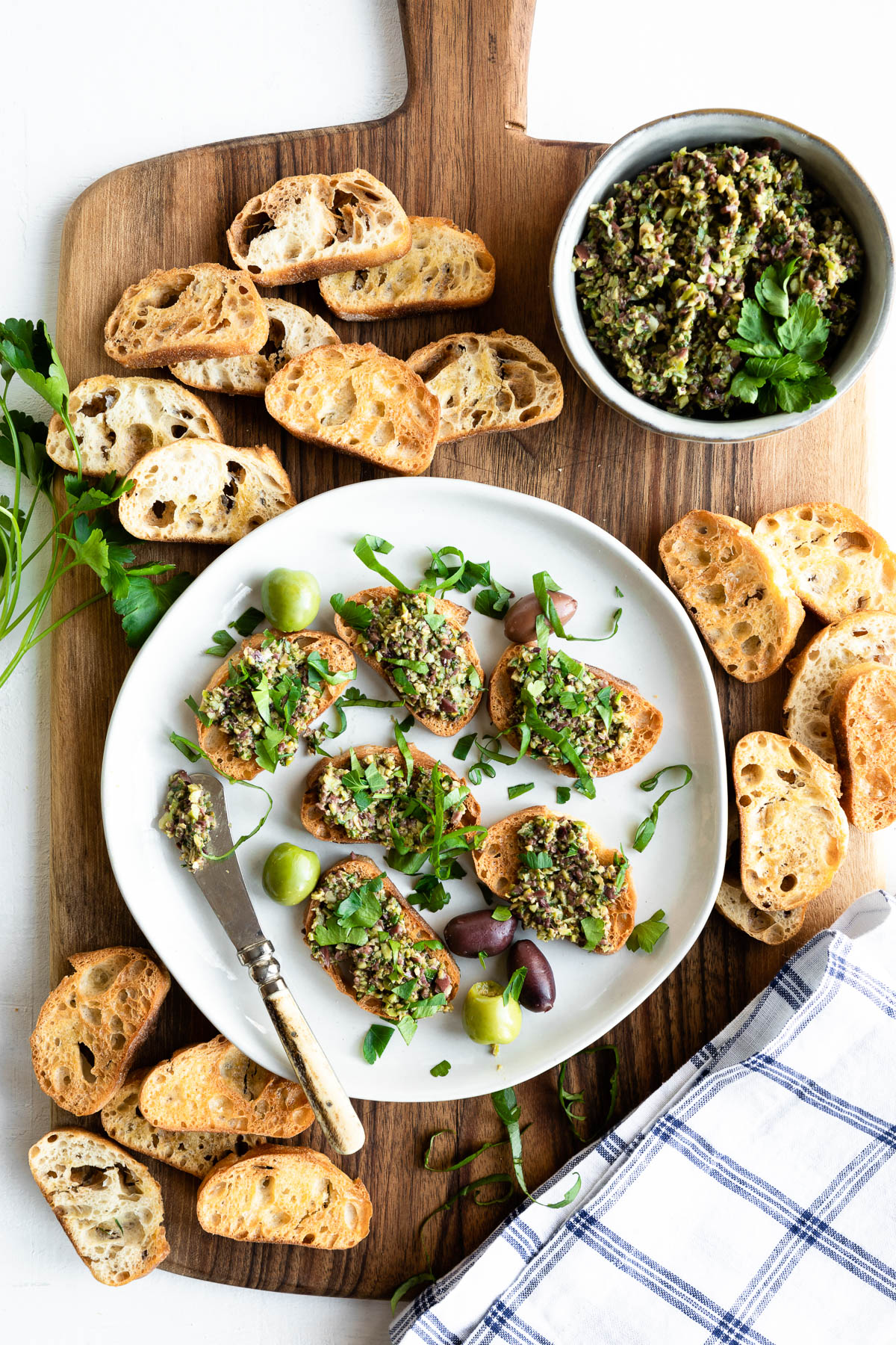 wooden board topped with crostini, tapenade and a plate full of appetizers already put together.