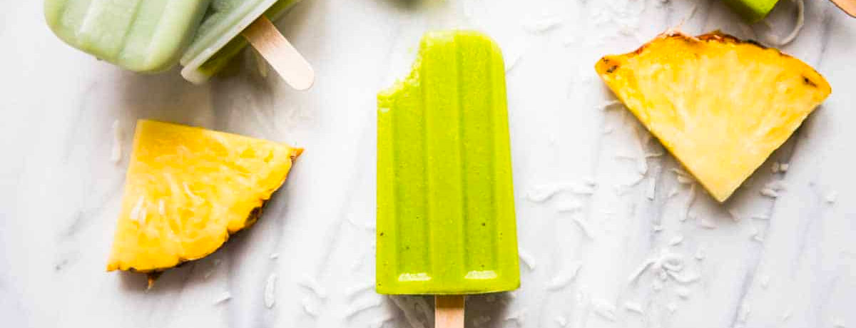 bright green smoothie popsicle with pineapple wedges next to it