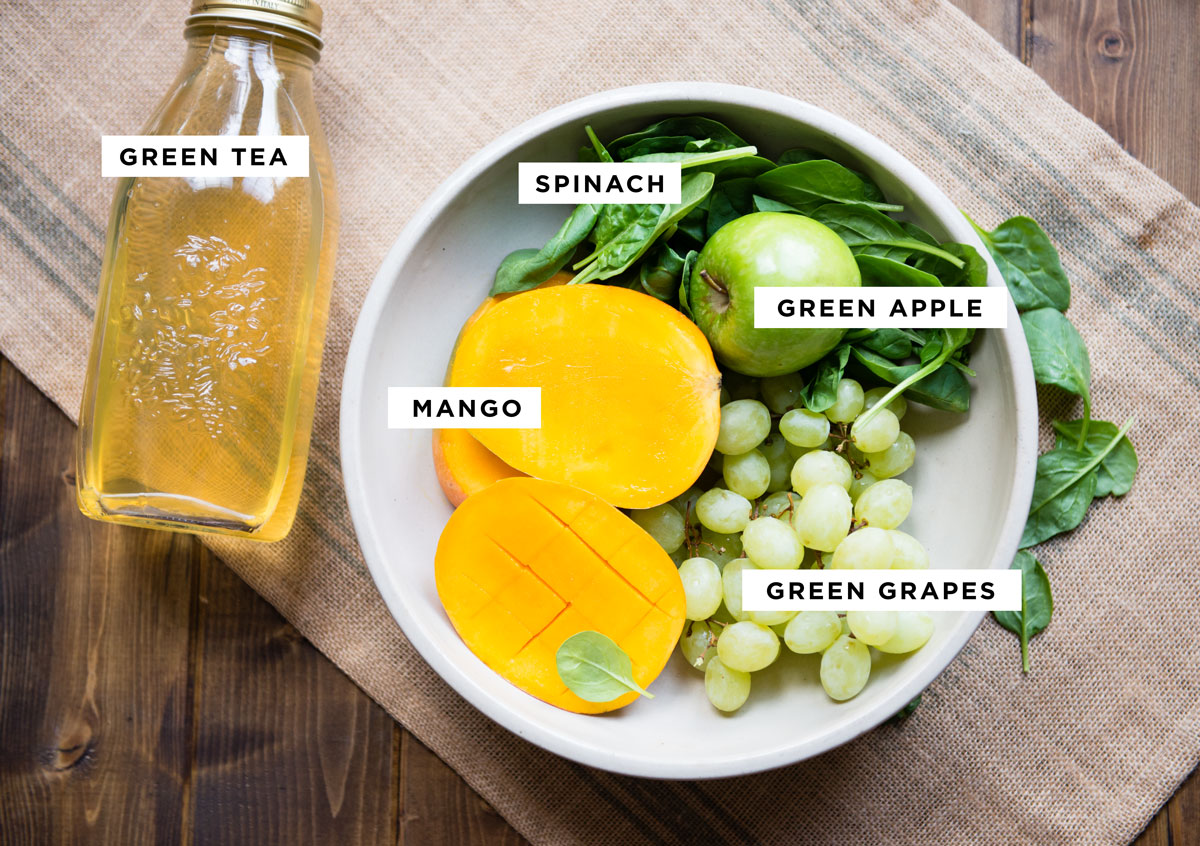 labeled ingredients for a healthy smoothie including green tea, spinach, green apple, mango and green grapes.