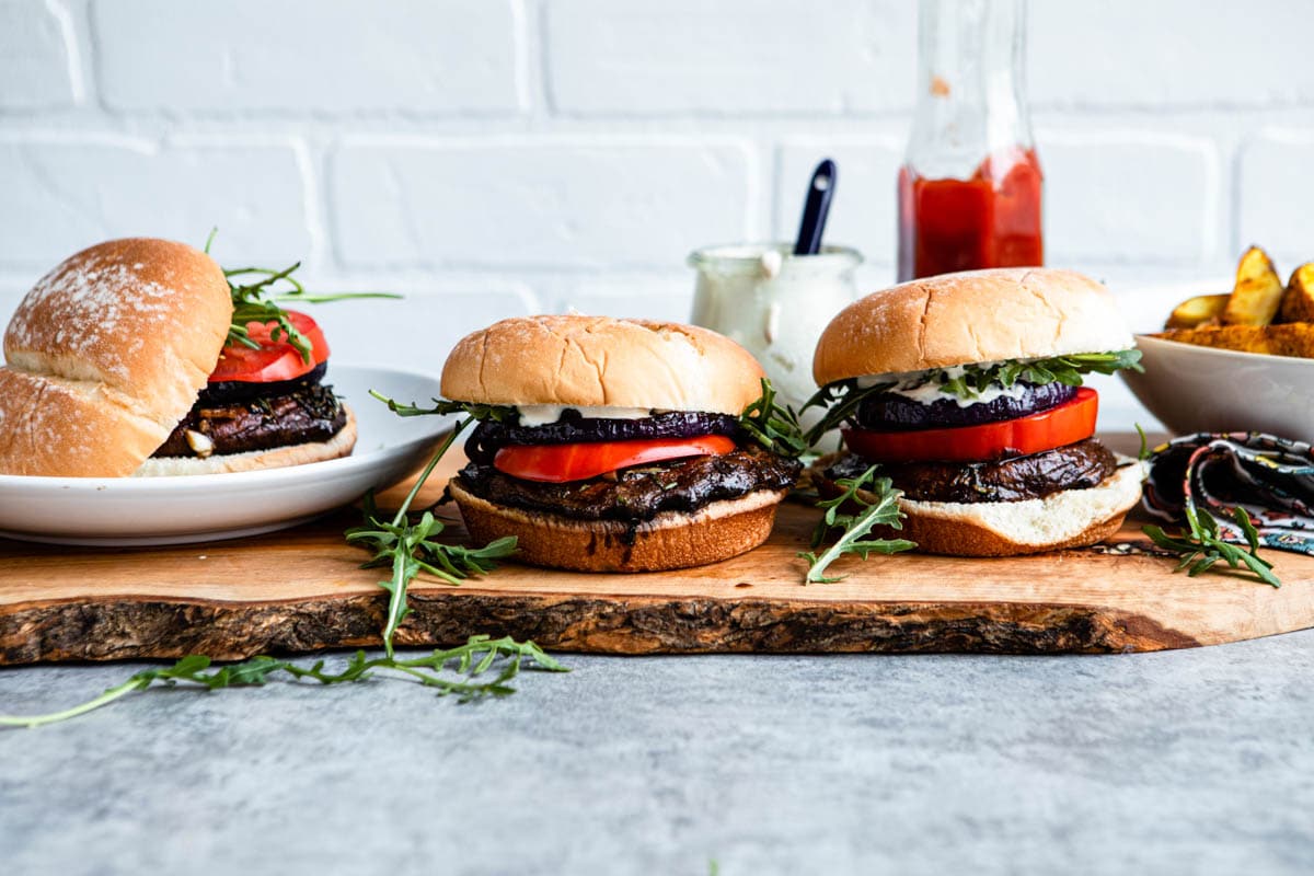 3 plant-based burgers on a counter loaded with arugula, tomatoes, garlic aioli and mushrooms.