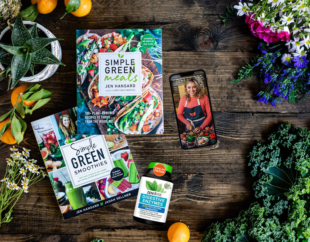 An image of healthy-living tools, including two green smoothie books, a bottle of digestive enzymes, and a phone with a picture of someone preparing vegetables.