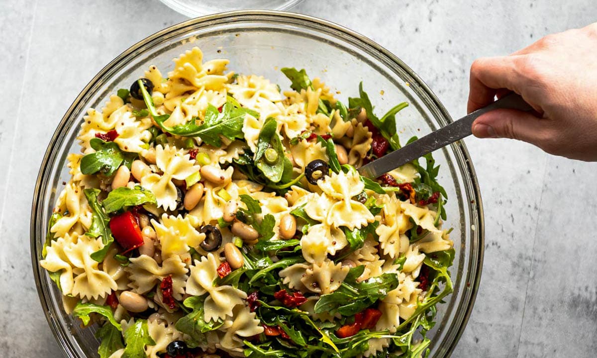 serving pasta salad as a fresh BBQ side in a glass bowl with a stainless steel serving spoon.