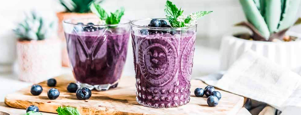 two blueberry smoothies in fun glasses with sprigs of mint on top