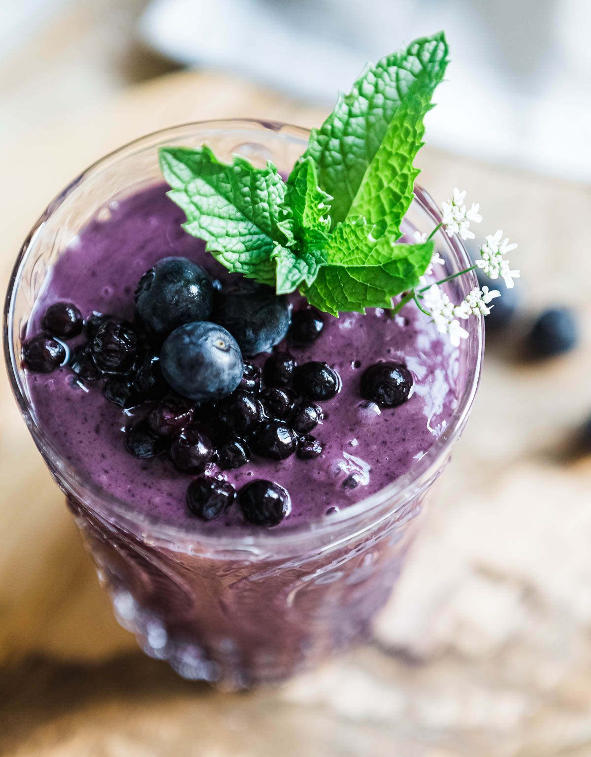 healthy blueberry smoothie in a glass topped with blueberries, fresh mint and flowers.