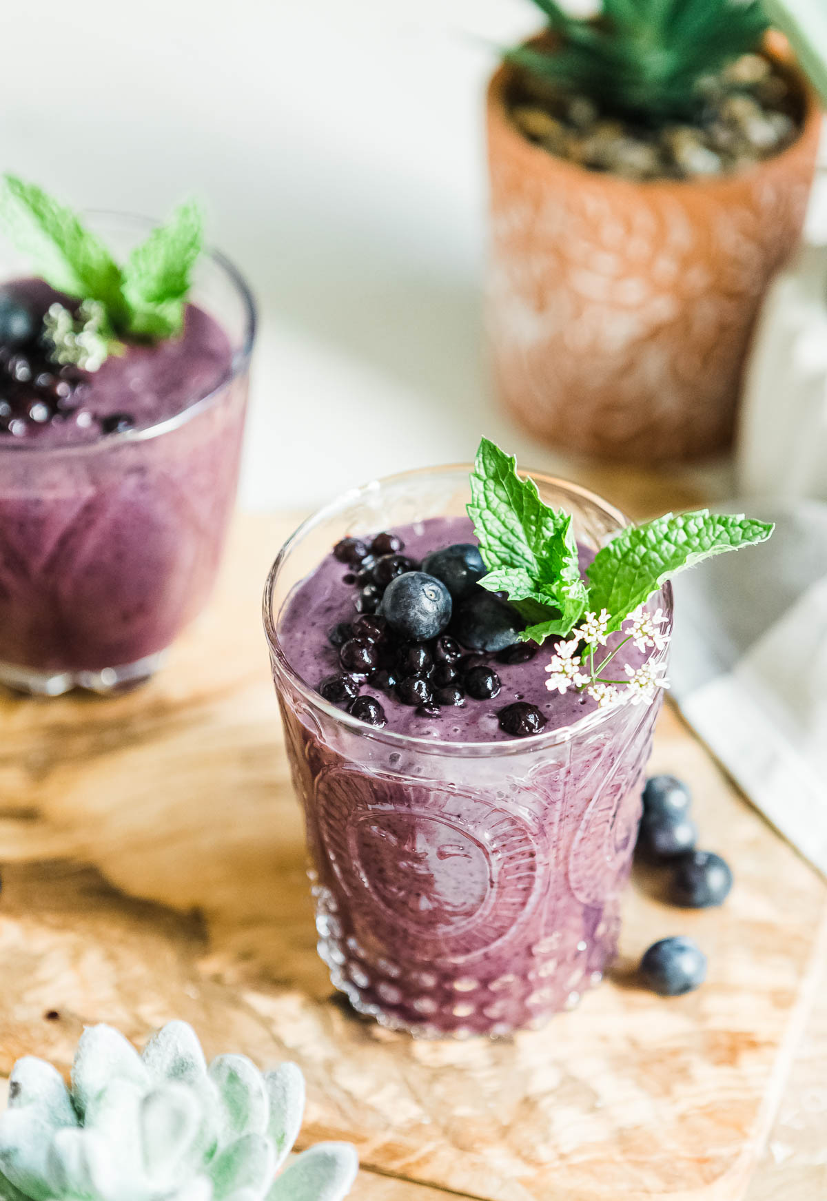 2 purple smoothies topped with fresh fruit and mint sprigs.