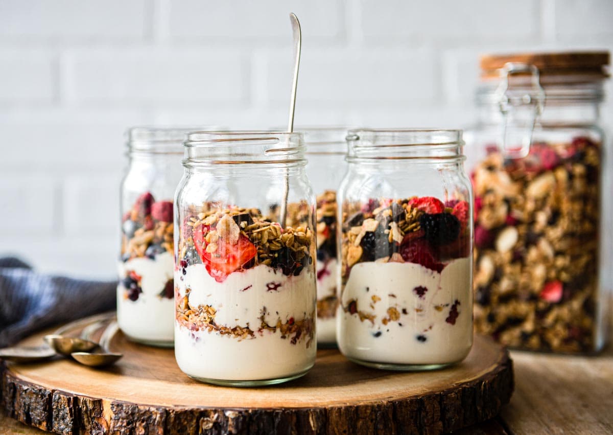 homemade yogurt parfaits in 4 glass jars on a wooden platter to serve at a healthy brunch.