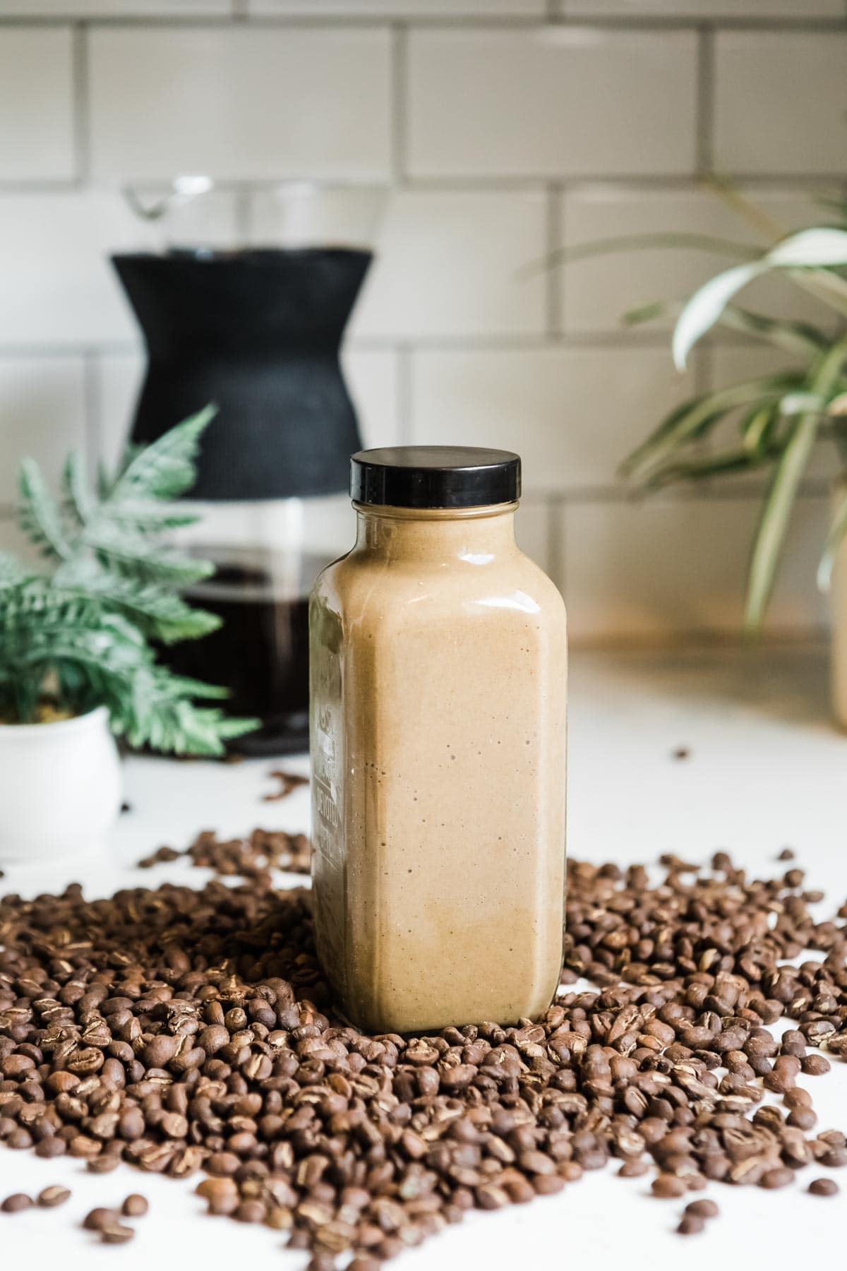 coffee smoothie in a glass jar with black lid surrounded by a pile of coffee beans.