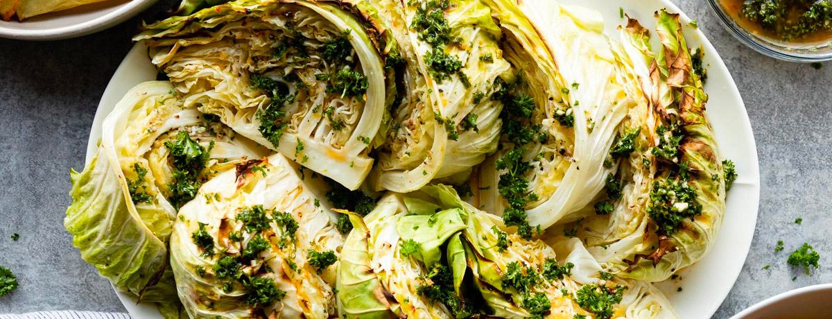quartered and cooked heads of cabbage on a plate with seasoning on top
