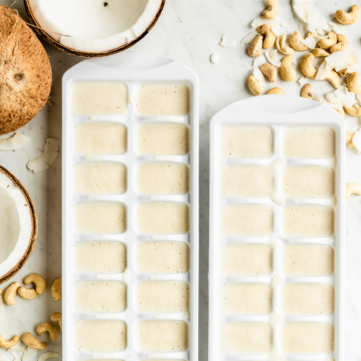 Two white ice cube trays filled with frozen Healthy Fats Smoothie cubes on a white countertop.