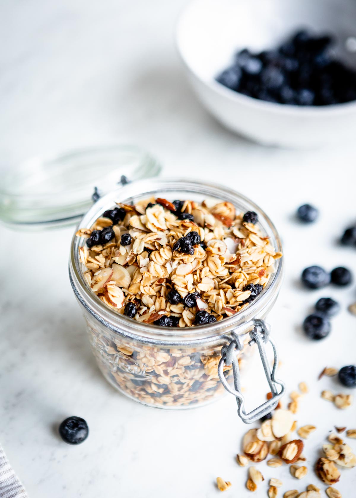 healthy granola in glass jar with fresh blueberries on counter.
