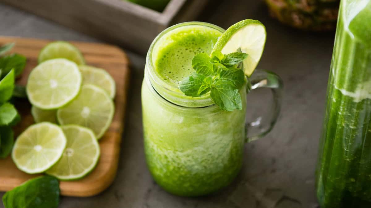 Healthy green smoothie with lime and mint in a glass jar on a gray surface.