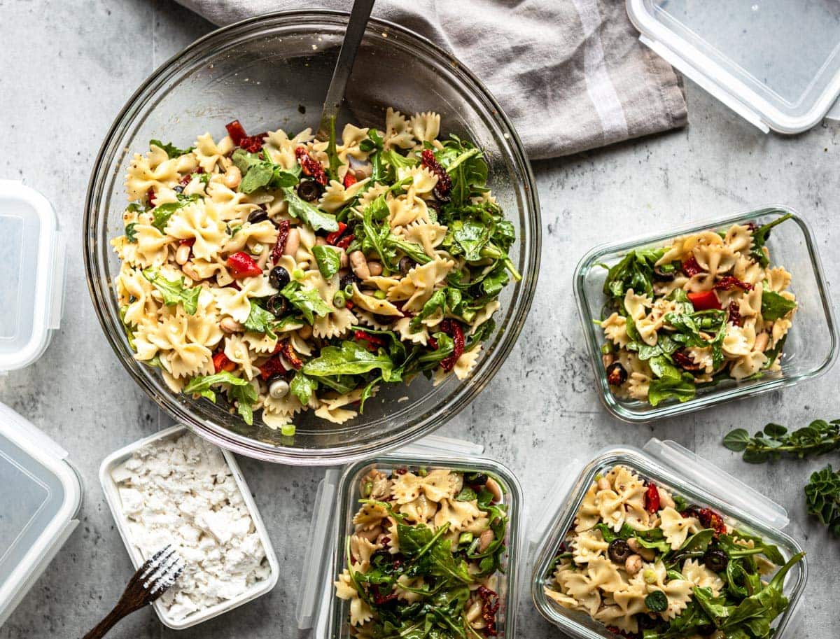 large glass bowl of healthy pasta salad with 3 glass containers for left overs and a container of vegan feta.