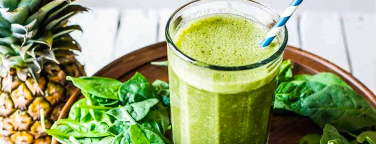 green smoothie with blue and white striped straw sitting on a bed of spinach with wooden background