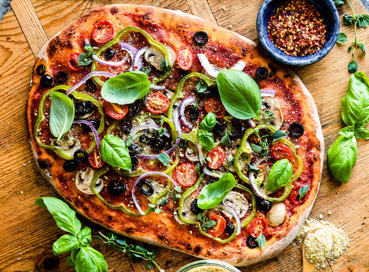freshly made veggie pizza topped with fresh basil, green onions, olives, tomatoes and red onion.