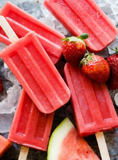 Healthy watermelon popsicles surrounded by fruit and ice