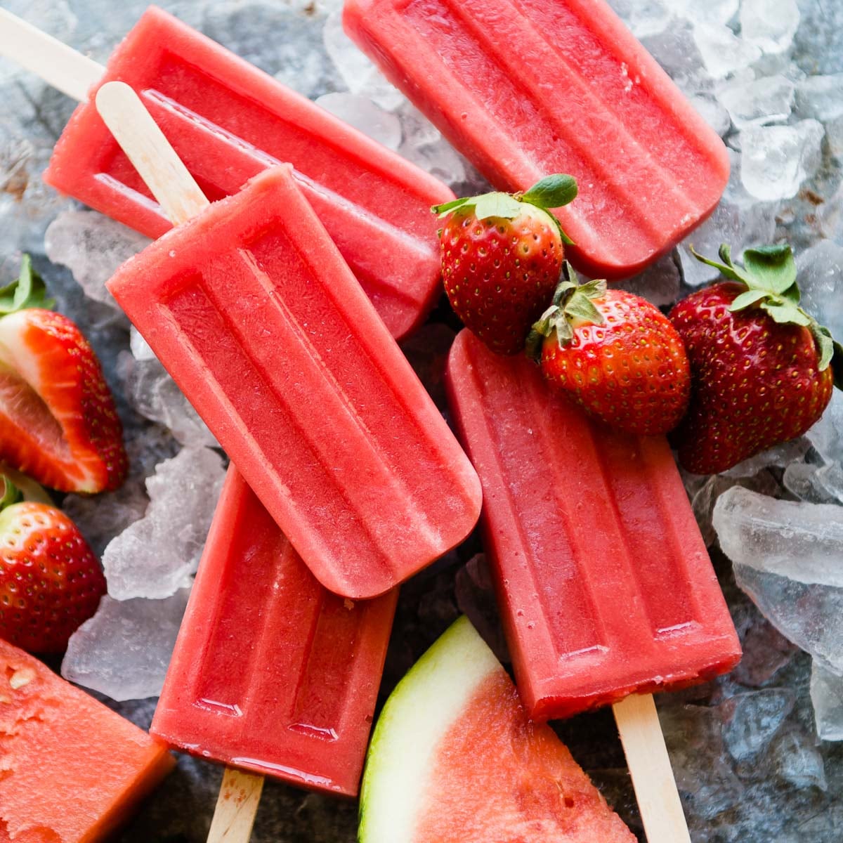 Healthy watermelon popsicles surrounded by fruit and ice