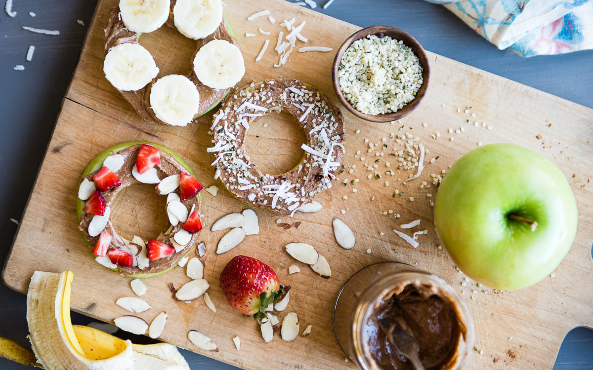 best snacks for weight loss including apple rings topped with nut butter, fresh fruit, coconut flakes, hemp hearts and almond slices.
