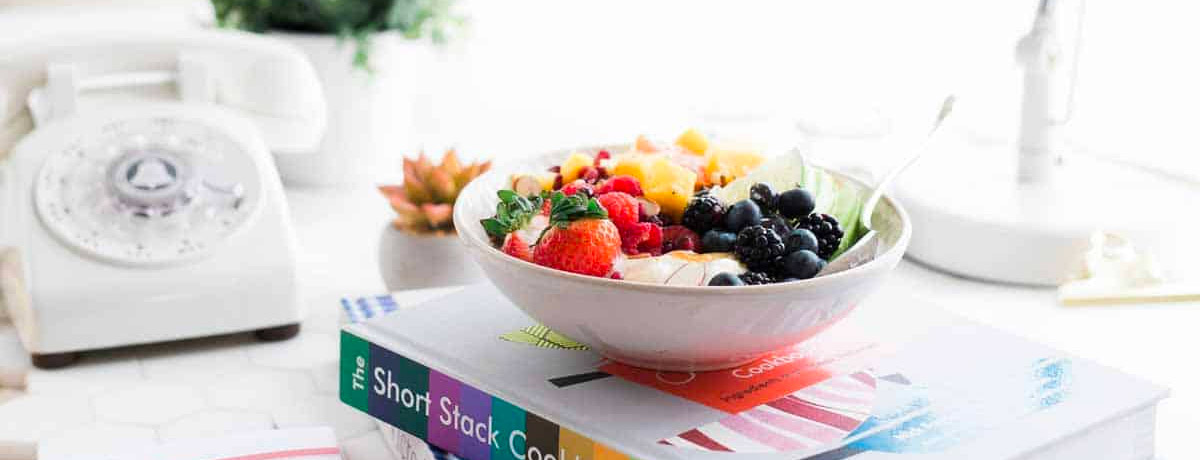 snack bowl with mixed fruits sitting on a books and a phone in the background