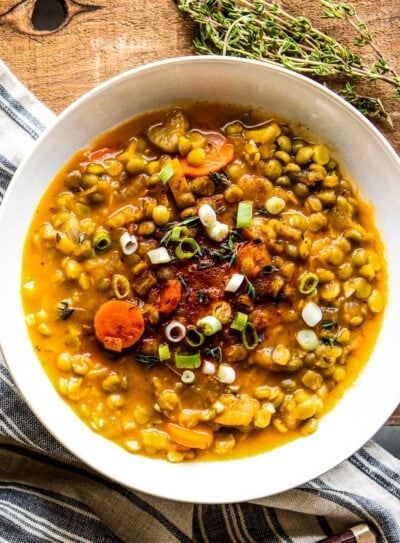 A bowl of healthy lentil soup with vegetables and green onions.