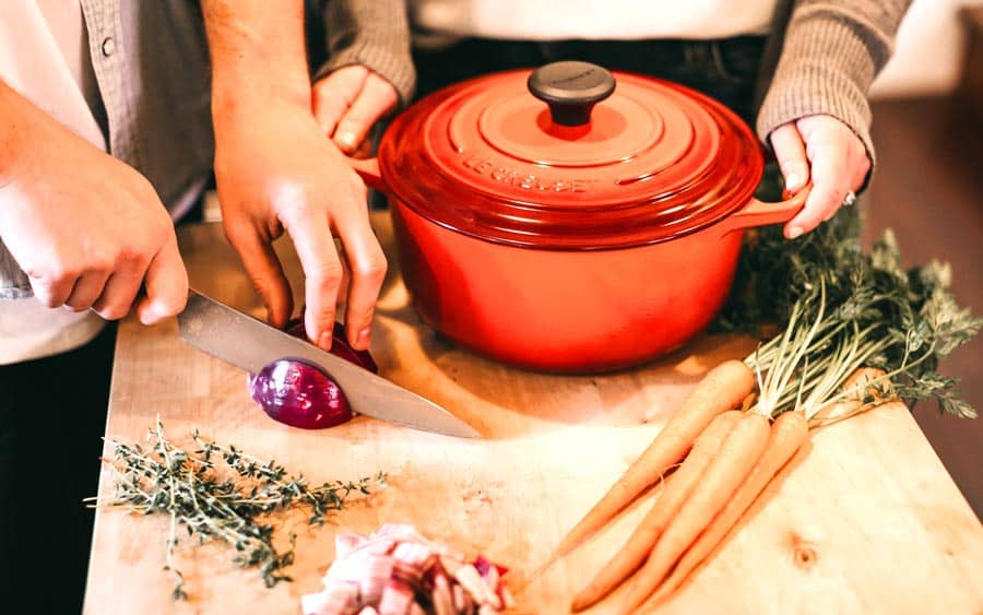 family prepping purple onions, carrots and herbs to put into a red stock pot.