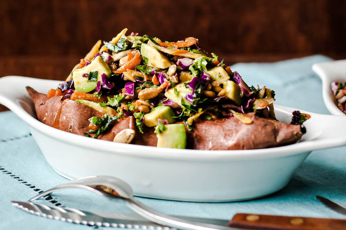 loaded baked sweet potato topped with kale slaw in an oval dish.