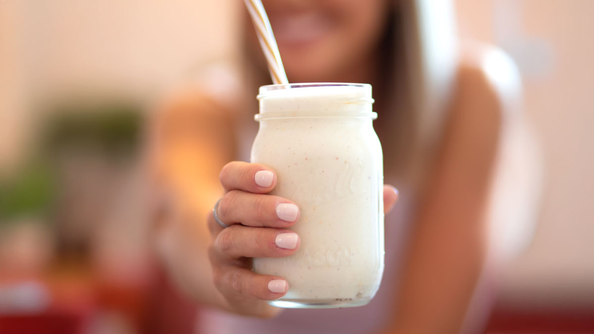 Girl holding a glass of vanilla protein shake with gold straw.