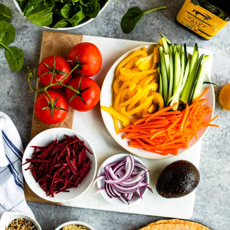 marble and wood cutting board topped with various vegetables in white bowls.
