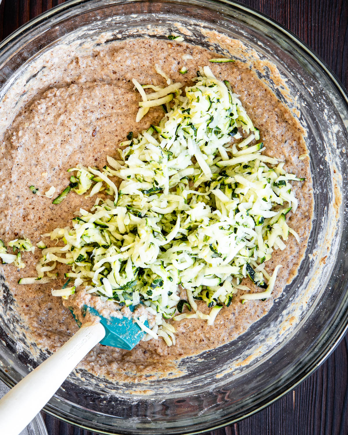 stirring shredded zucchini into a glass bowl of other ingredients.