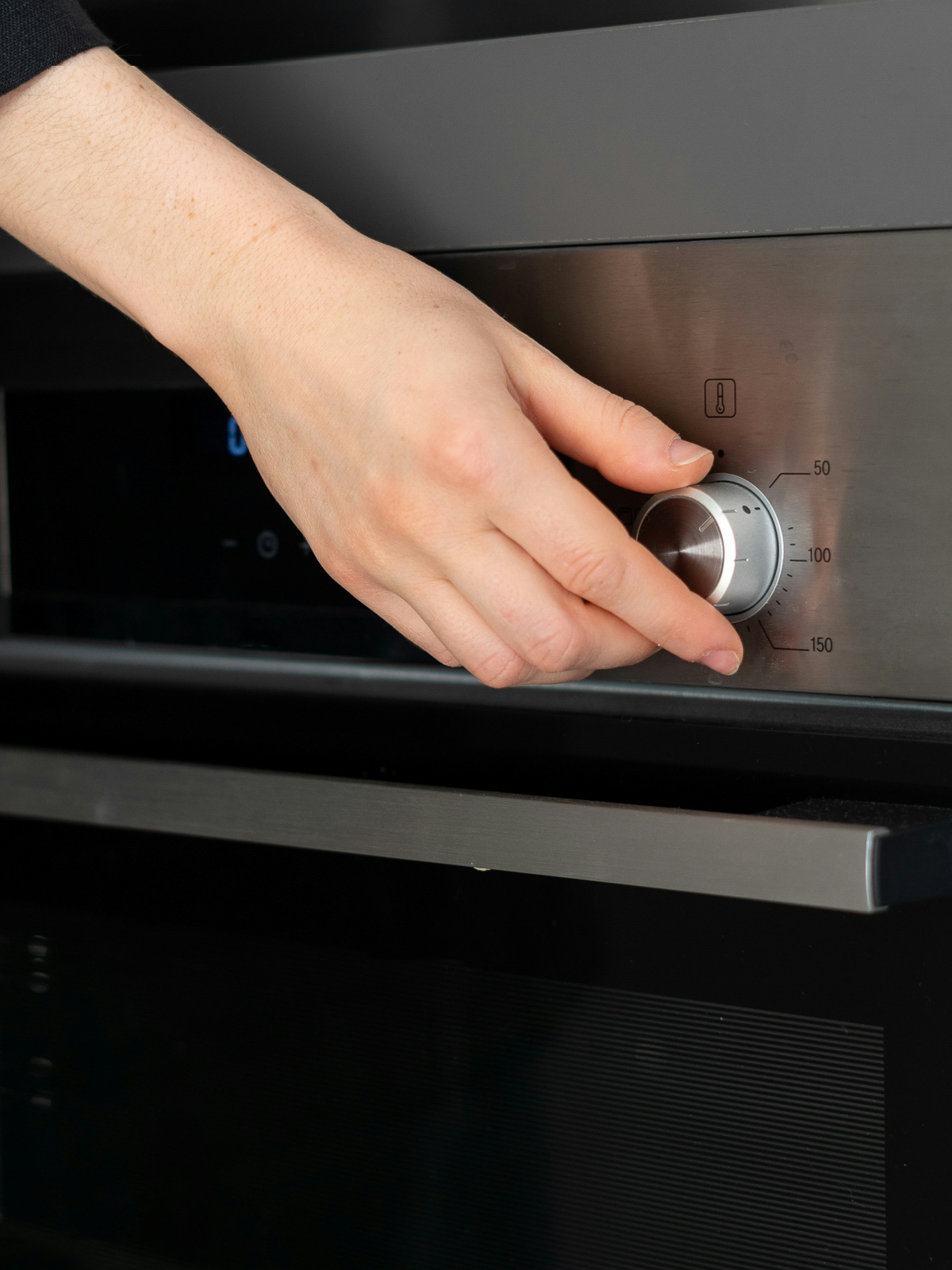 A hand reaching for a knob to preheat the oven.