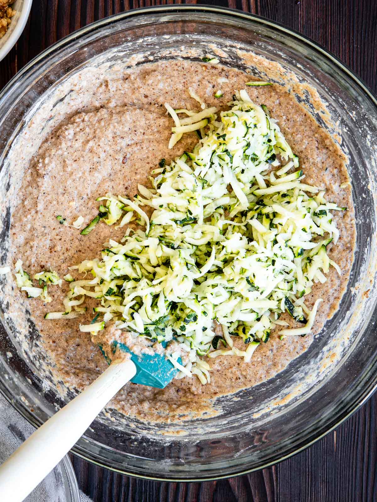 stirring shredded zucchini into a glass bowl of other ingredients.