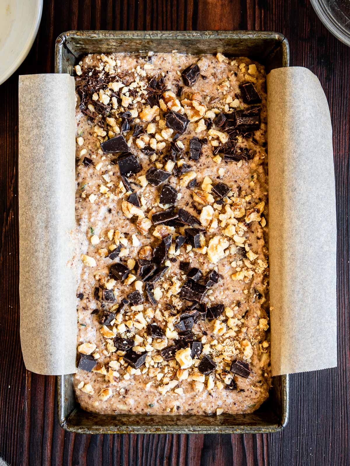 loaf pan with zucchini bread batter topped with chocolate chunks ready to be baked.