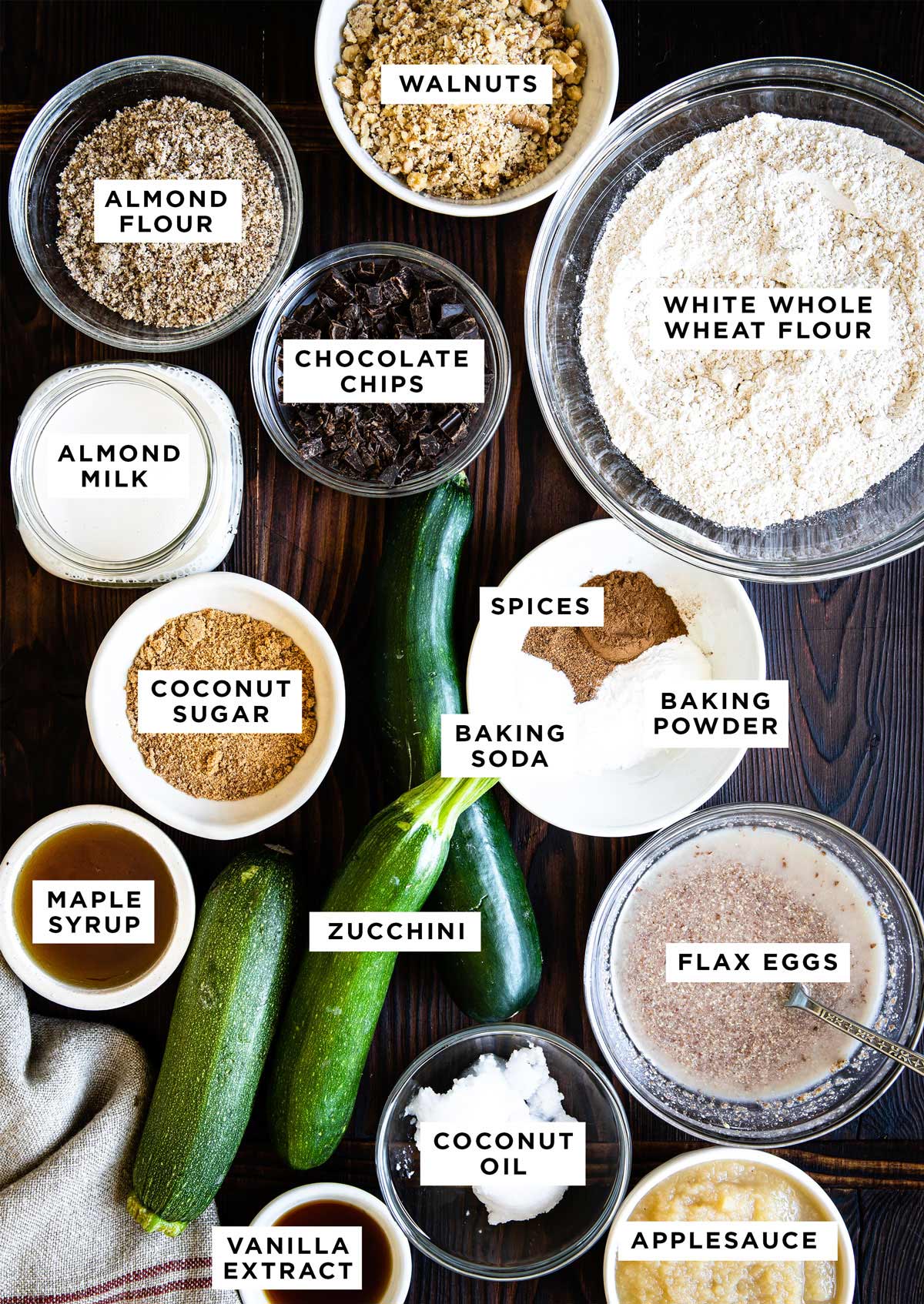 Labeled ingredients for healthy zucchini bread recipe on walnut colored wood countertop.