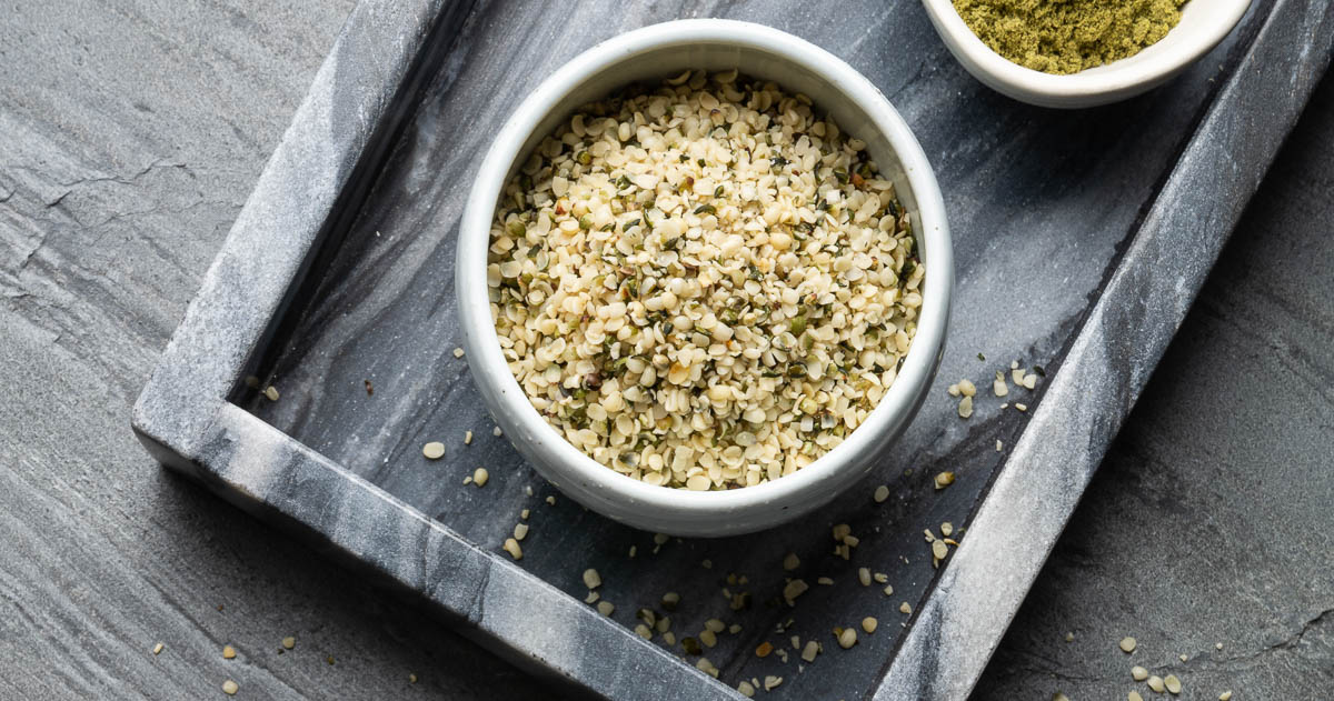 a marble tray with a container of hemp seeds in a white bowl.